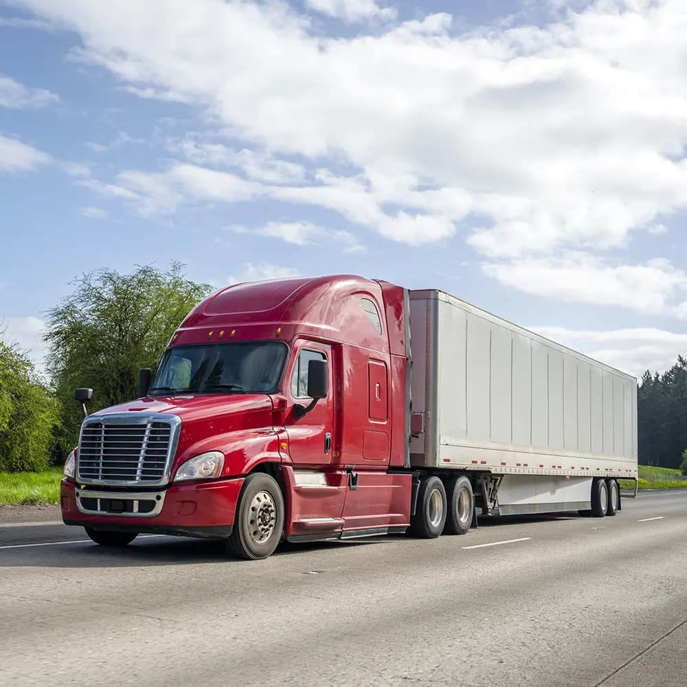 Red semi-truck hauling a white trailer on the highway