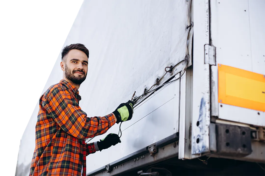 Man wearing plaid shirt tying down cover on pallet drop trailer at warehouse loading bay