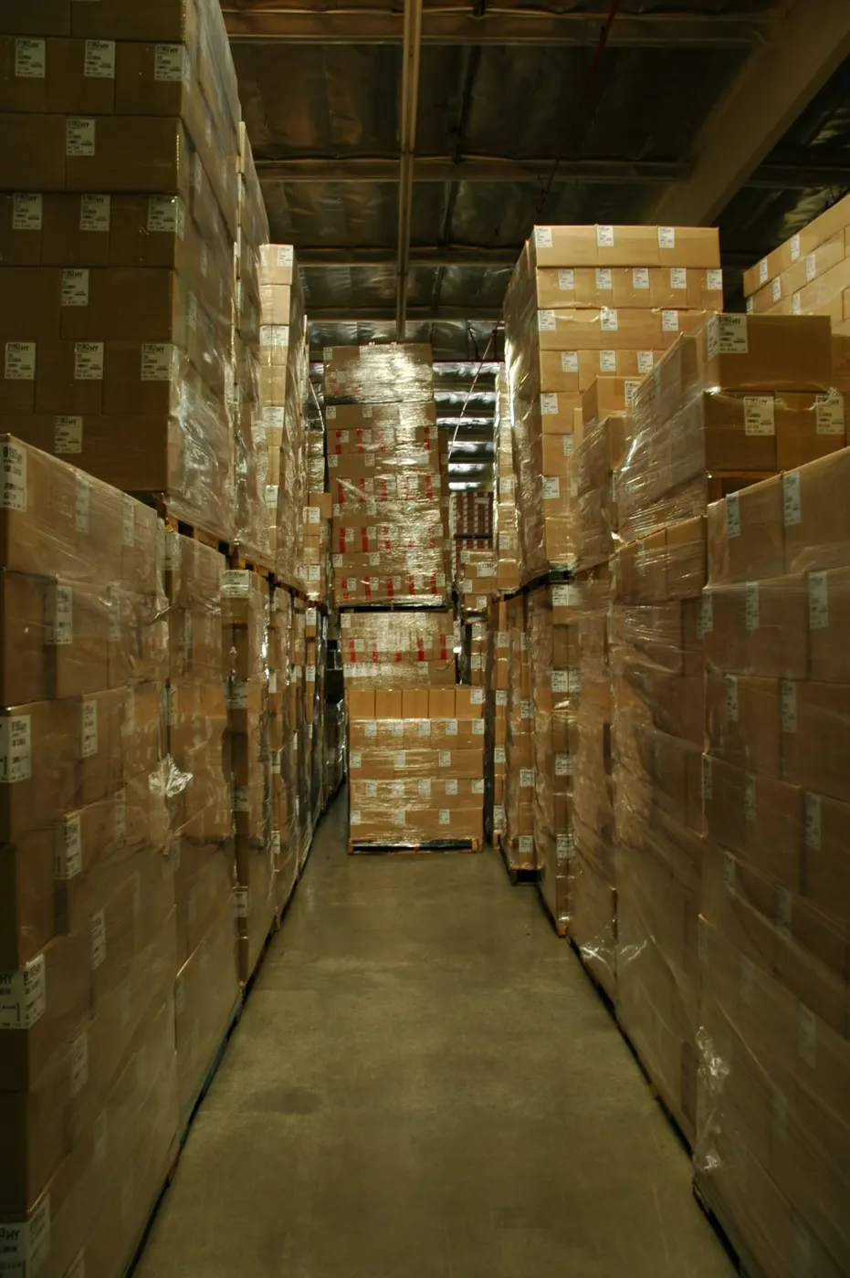 Warehouse aisle lined with shrink-wrapped boxes on pallets