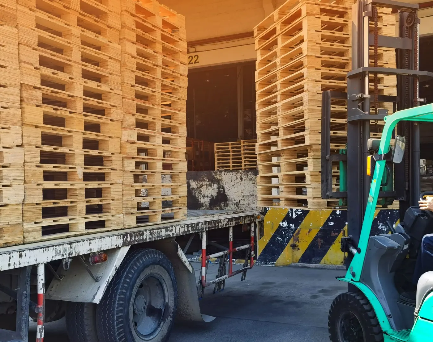 Forklift loading stacked wood pallets onto a truck for delivery
