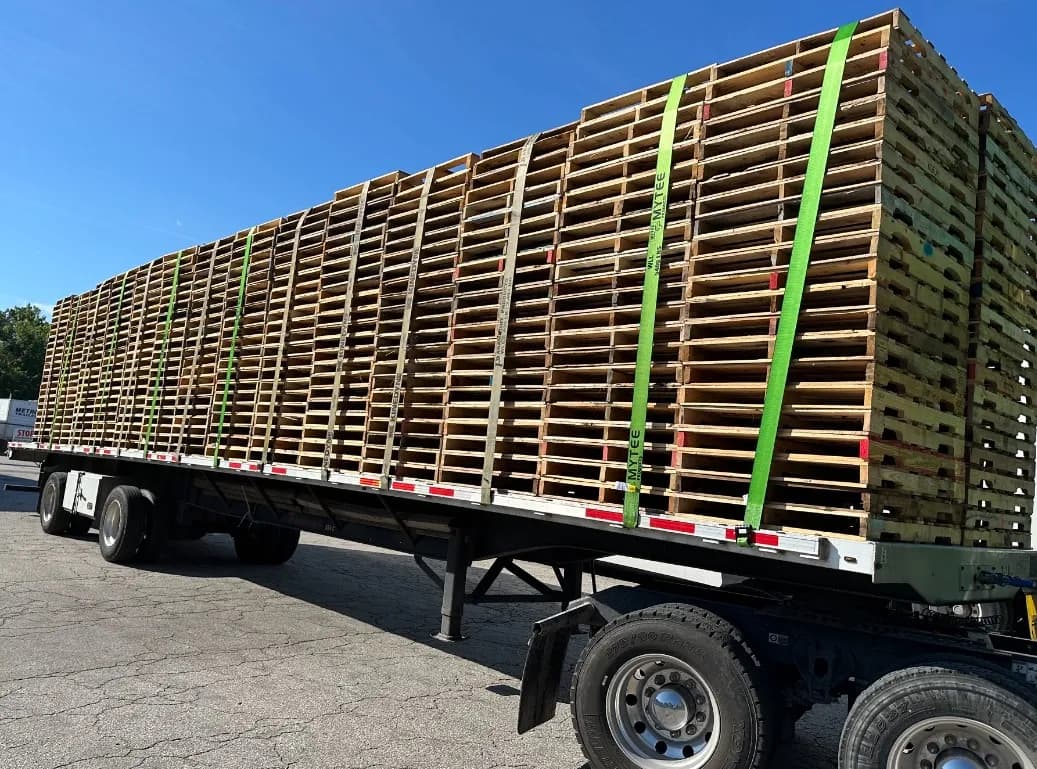 Flatbed trailer loaded with stacks of 48x40 wooden pallets strapped down for delivery