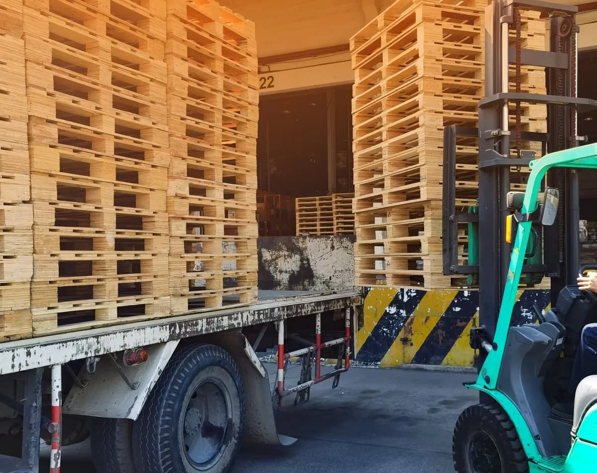 Forklift loading stacked wooden pallets onto a truck at a loading dock