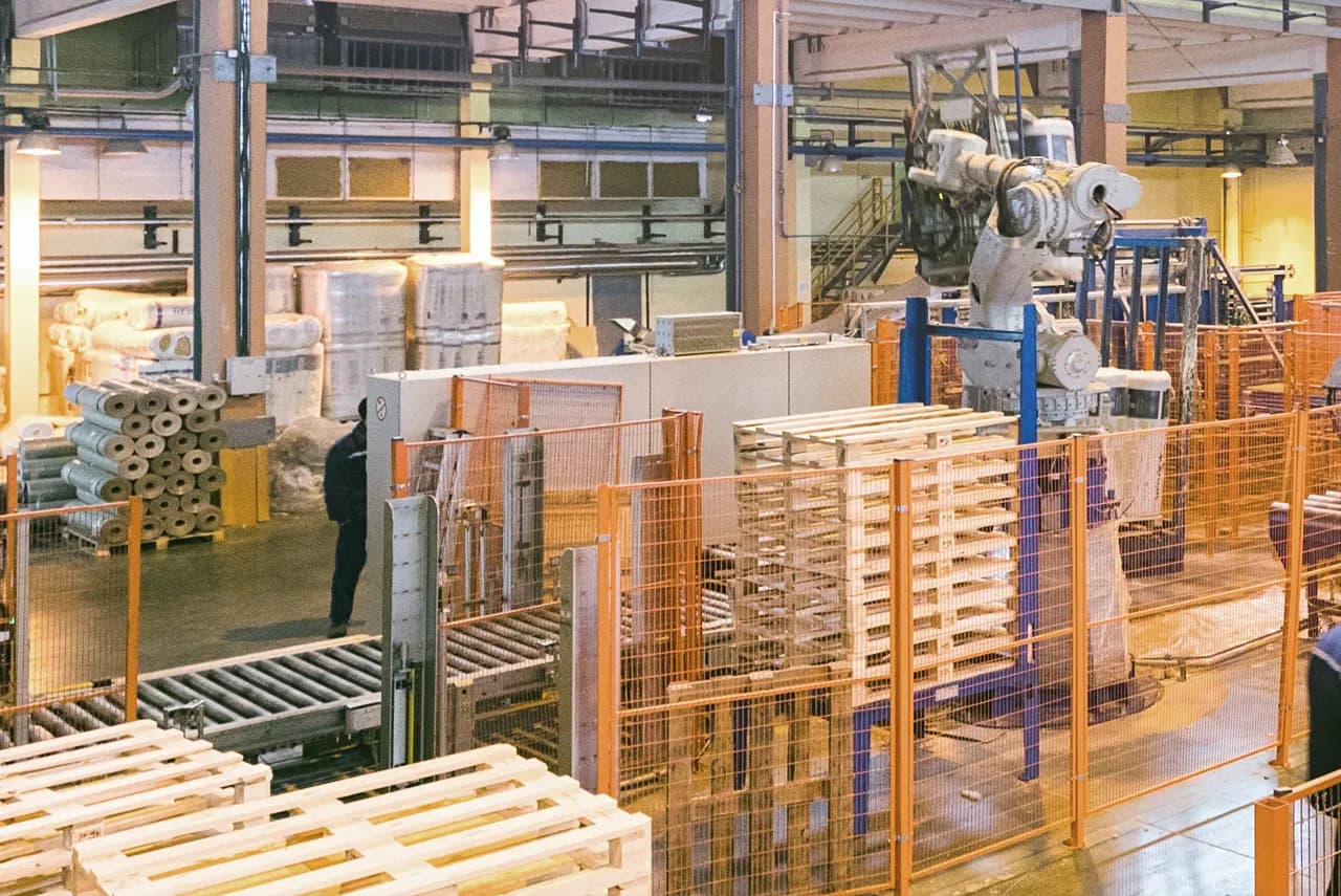 Pallet factory with a robotic arm stacking new light wood pallets beside a conveyor