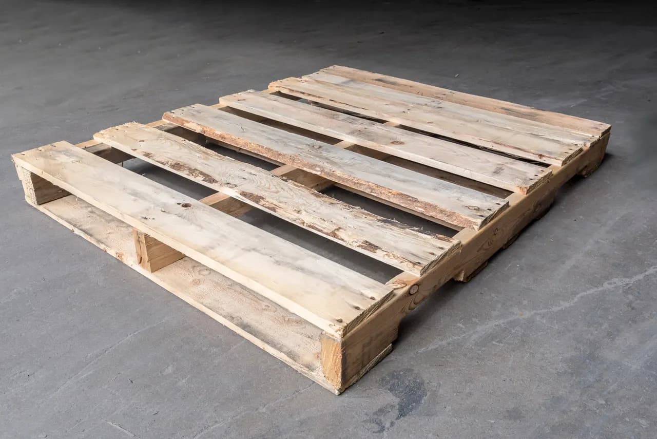 Used wood pallet with worn, weathered pale boards on a grey concrete floor