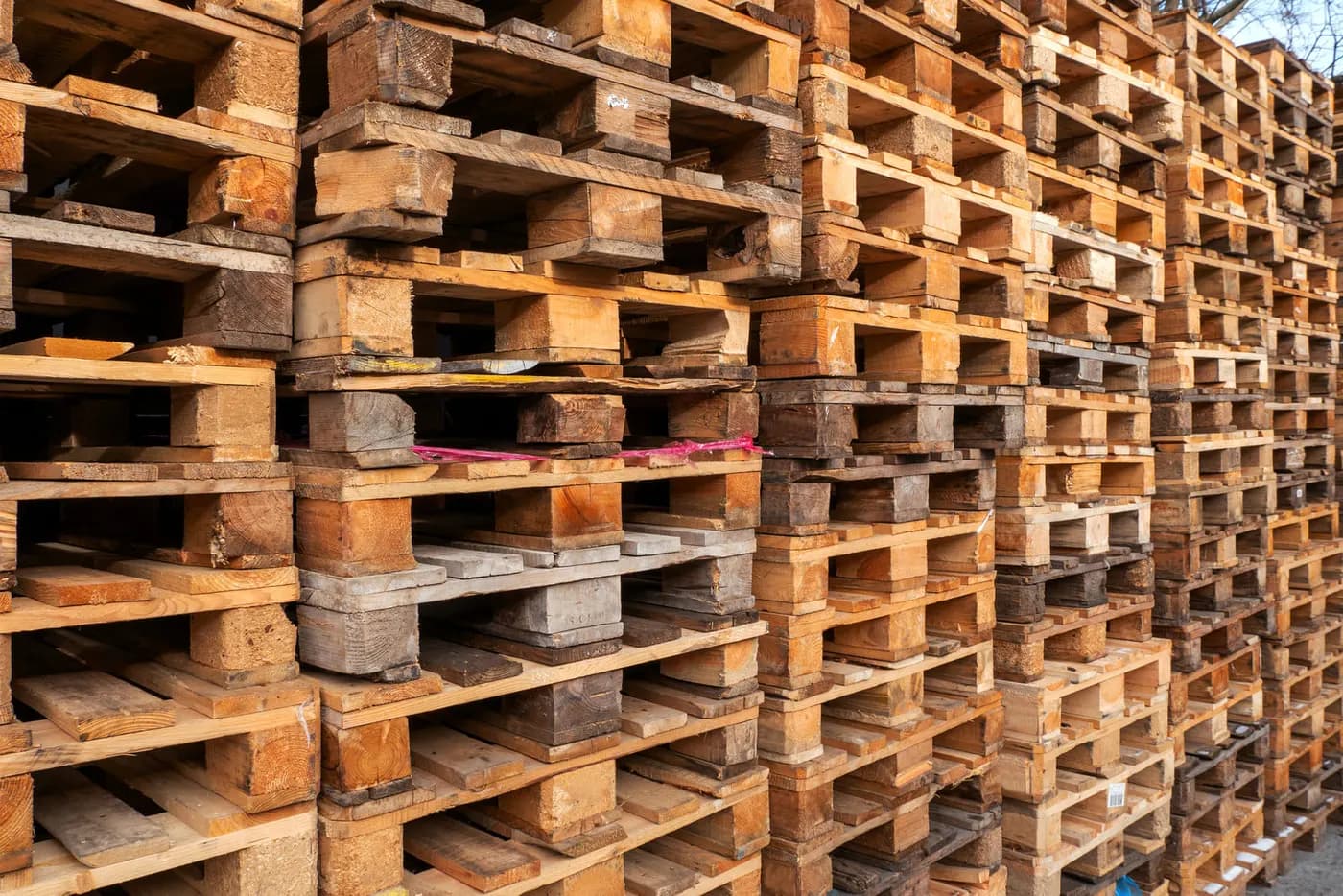 Tall stacks of weathered used wood pallets in warm brown tones