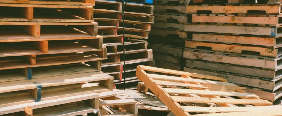 Piles of used wood pallets stacked against a wall, ready for resale